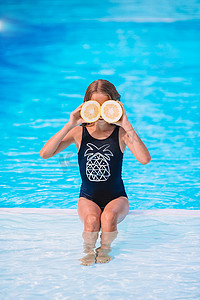 在背景游泳池的眼睛附近用柠檬半遮住眼睛的小女孩