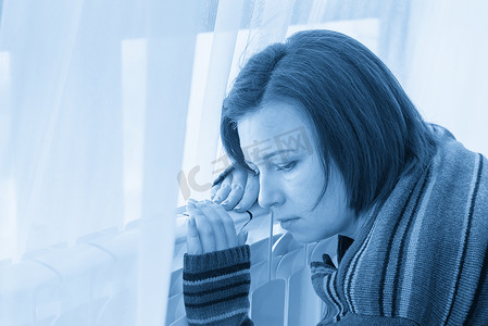 冷色调摄影照片_穿着套头衫的女人坐在加热器散热器附近并拥抱它