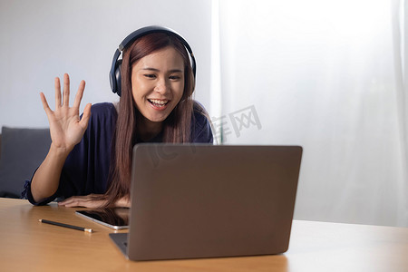 戴着耳机的年轻亚洲女学生享受使用笔记本电脑在家在线学习的便利，有效地与老师互动。
