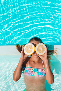 在背景游泳池的眼睛附近用柠檬半遮住眼睛的小女孩