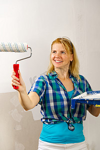 手绘房屋装饰摄影照片_女人用白色的油漆滚筒手绘墙。