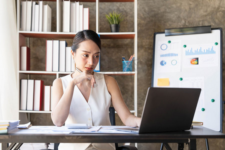 亚洲女商人使用笔记本电脑，在办公室工作，在办公桌上使用计算器文档，进行规划分析财务报告、商业计划投资、财务分析概念。