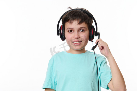 新学期摄影照片_英俊的小男孩在视频课上戴着耳机，对着镜头微笑。