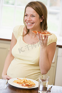 孕妇在厨房吃炸薯条和比萨微笑