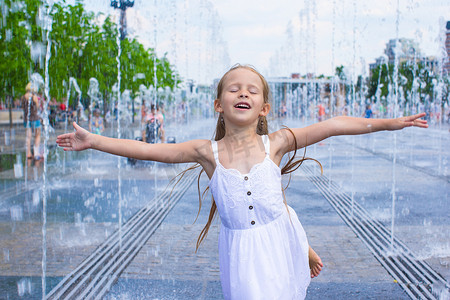 在阳光明媚的炎热日子里，快乐小女孩的肖像在街边喷泉里玩得开心