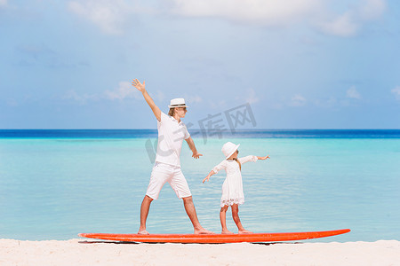 爸爸和孩子运动摄影照片_暑假期间爸爸和孩子在冲浪板上的家庭