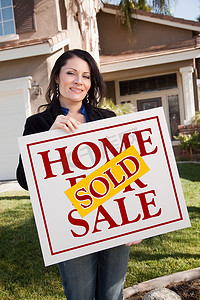 女人拿着出售的房地产标志在房子前面