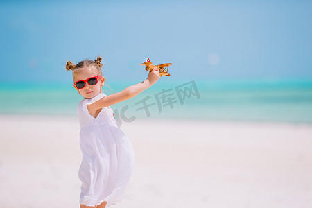 白色沙滩上手拿玩具飞机的快乐小女孩