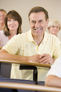 男子坐在成人教室里，背景是学生（选择性焦点）