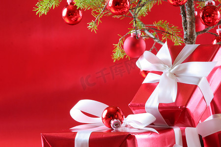 深红色背景摄影照片_优雅的红色礼物在圣诞树下，深红色背景。