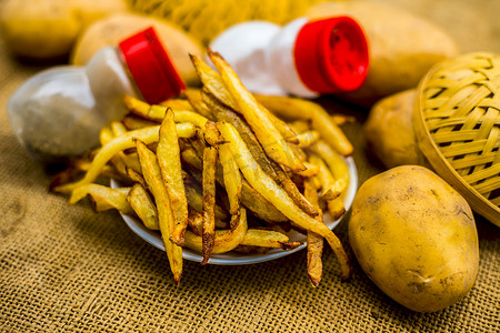 炸包摄影照片_新鲜炸薯条，在黄麻袋表面撒上黑胡椒和盐，还有一些生土豆。