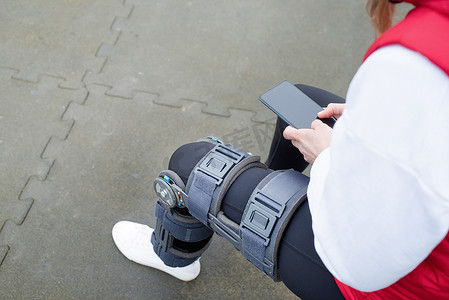 长款包腿护膝摄影照片_在公园锻炼腿部手术后戴护膝或矫形器的妇女