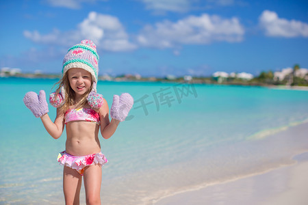 热带海滩上戴着温暖针织帽和手套的可爱小女孩