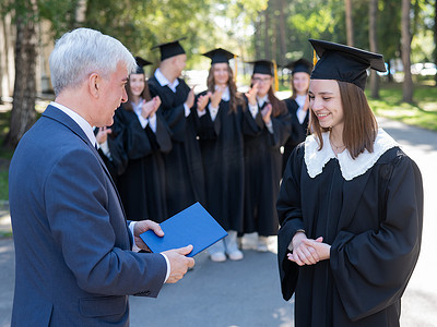 老师在户外与学生握手并颁发毕业证书。