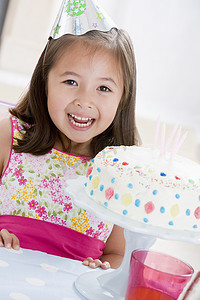 派对帽摄影照片_戴着派对帽、面带微笑的生日蛋糕的年轻女孩