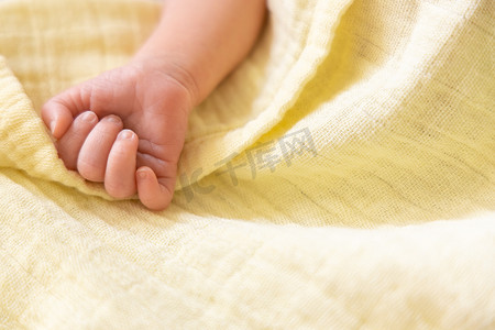 新生儿白种人早产婴儿手放在淡黄色柔软的平纹细布毯子上。