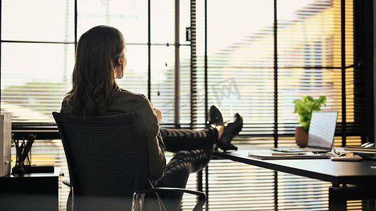 沉思的女商人坐在她的工作场所，望着窗外思考投资策略或项目成功