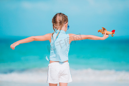 白色沙滩上手拿玩具飞机的快乐小女孩