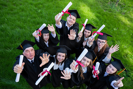 穿着长袍的毕业生在户外炫耀他们的毕业证书。