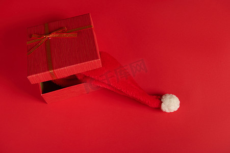 一个半开的圣诞礼盒的顶视图，里面有一顶圣诞帽，在红色背景中被隔离，带有复制广告空间