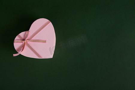 端午节礼摄影照片_一份浪漫的礼物，一个心形的粉红色礼盒，用于圣瓦伦丁节或妇女节，背景为绿色。