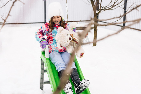 玩雪橇的孩子摄影照片_带着玩具泰迪熊的孩子坐在雪橇上。