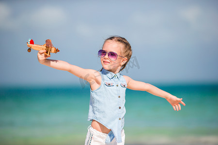 快乐的小女孩在沙滩上玩玩具飞机。