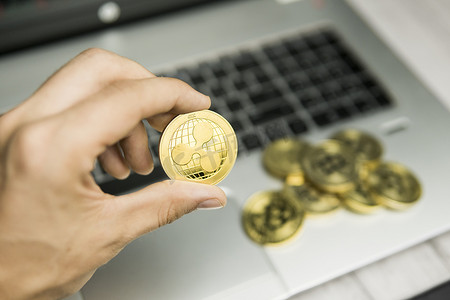 ripple摄影照片_男性商人手拿着 Ripple 硬币在笔记本电脑键盘和一堆金币的背景上。