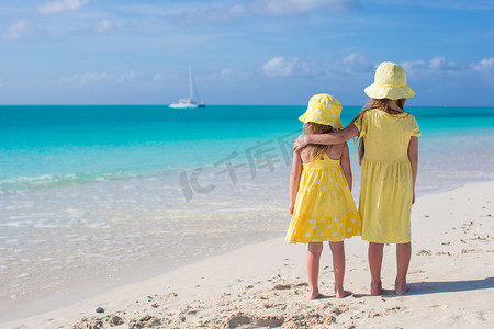 两个可爱的小女孩在白色沙滩上看海的背影