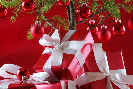深红色背景摄影照片_优雅的红色礼物在圣诞树下，深红色背景。