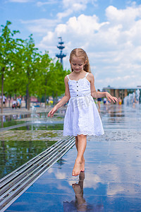 在炎热的阳光明媚的日子里，在开放的街道喷泉中行走的可爱小女孩