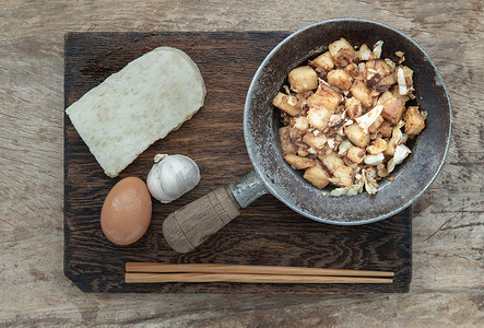 萝卜糕摄影照片_传统的炒软萝卜糕或炒萝卜糕（chai tow kway）在小蒸铁锅中，在质朴的旧木背景上用木筷子服务。