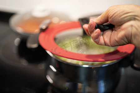 绿背景摄影照片_用开水或绿汤和风景蒸汽背光的电炉上的女性手打开锅盖。