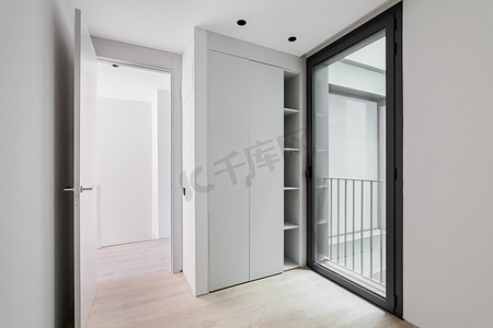 现代风格的入口大厅内部、中性白色走廊、木质浅色镶木地板、滑动衣柜和黑色铝框玻璃门，可通往街道。