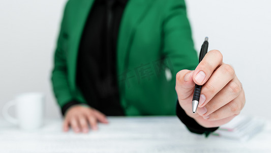 白西装白模特摄影照片_身穿绿色西装的男模特坐在白桌旁，用笔指着重要信息。