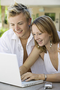 微笑迷人的夫妇坐在后院的桌子旁，使用笔记本电脑