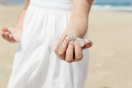 沙滩捡贝壳摄影照片_沙滩上拿着石头的女孩