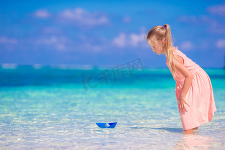 小纸船摄影照片_可爱的小女孩在绿松石海中玩折纸船