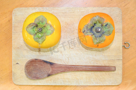 柿子文化摄影照片_砧板上的两个柿子和木勺