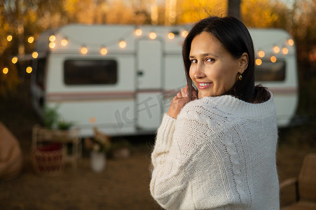 温暖的秋天，一位身穿白色针织毛衣的白人女性正在房车附近休息。