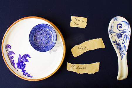美味，美味，晚餐时间的字母和文字，空的蓝色餐具，蓝色桌子上的碗和盘子。