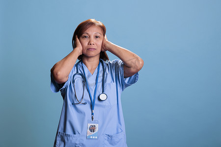 亚洲安静护士用听诊器遮住耳朵，表情严肃