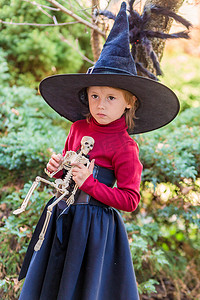 在万圣节派对上，穿着女巫服装的小女孩拿着一具骷髅