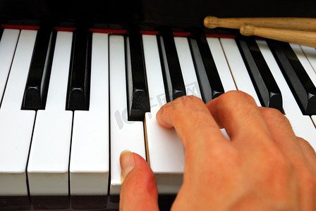 右手用鼓棒在钢琴键盘上弹奏