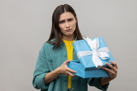 深色头发的女人打开蓝色礼盒，用悲伤的表情看着相机。