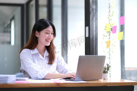 财务办公摄影照片_亚洲女商人使用笔记本电脑，在办公室工作，在办公桌上使用计算器文档，进行规划分析财务报告、商业计划投资、财务分析概念。