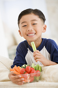 芹菜炒肉丝摄影照片_小男孩在客厅里微笑着吃一碗蔬菜