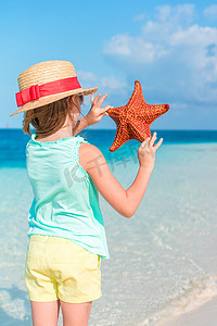 海星可爱摄影照片_白色空荡荡的沙滩上抱着巨型红海星的可爱小女孩