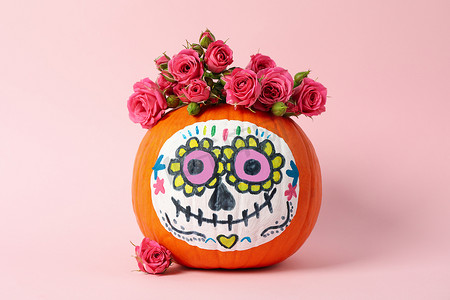 头骨和鲜花摄影照片_南瓜与卡特里娜头骨化妆和粉红色背景中的花朵