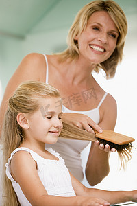 梳头发的人摄影照片_浴室里的女人梳着年轻女孩的头发